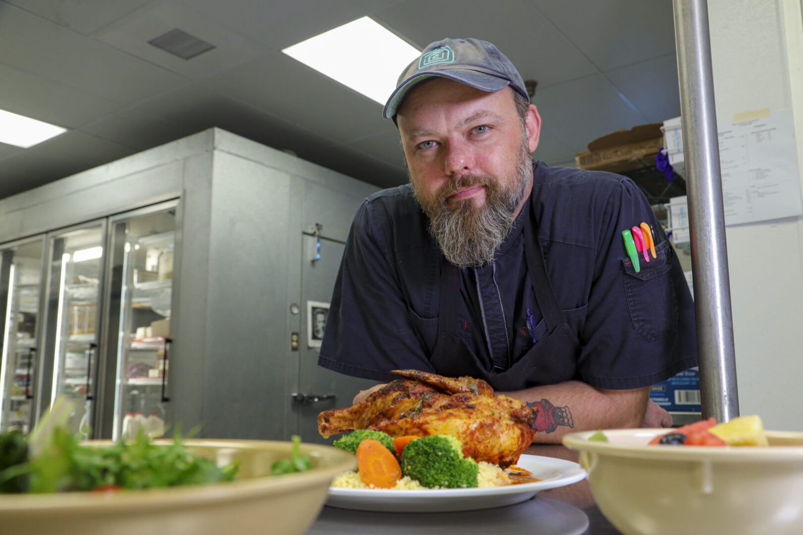 Bearded chef leaning over roasted chicken