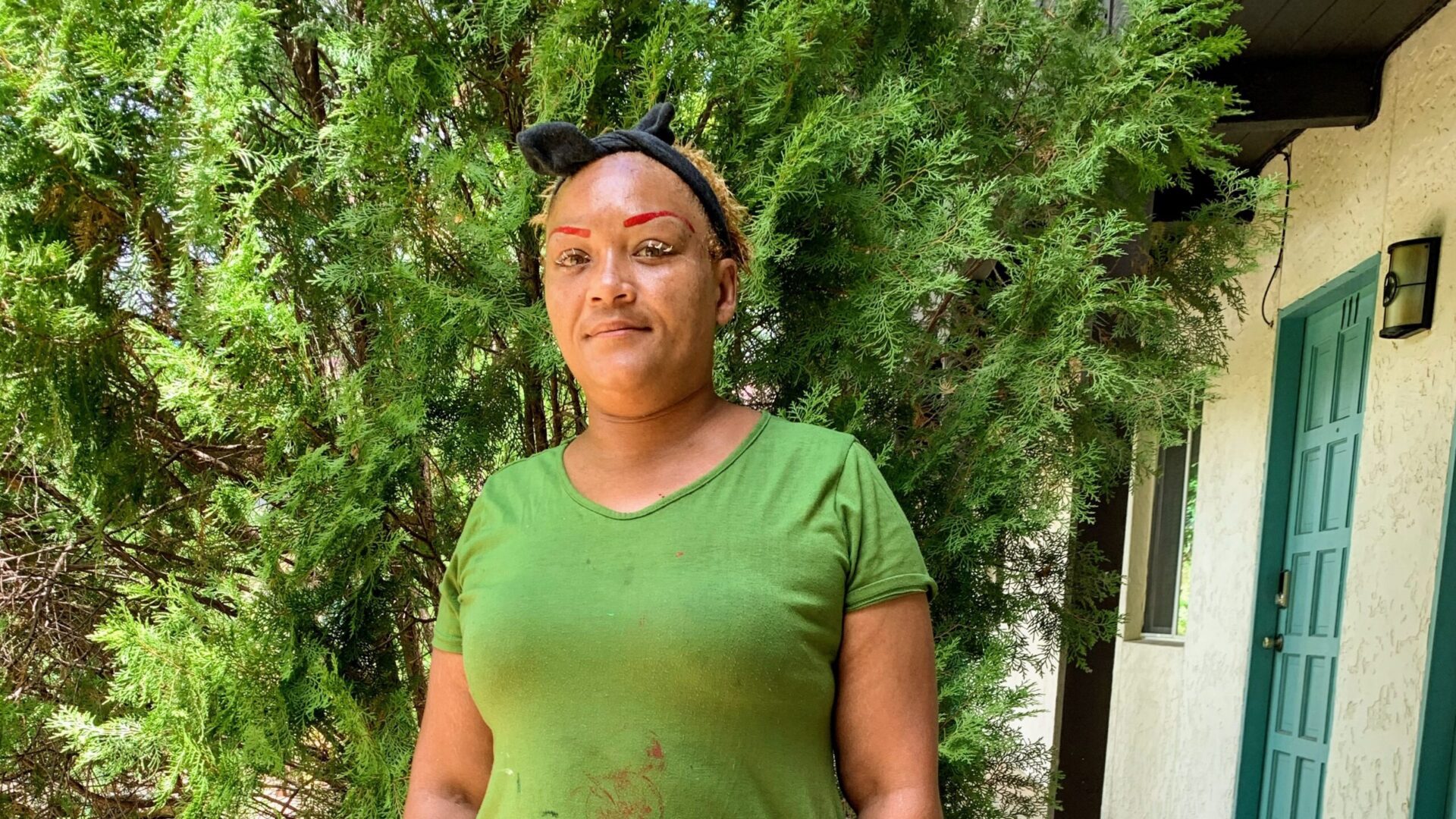 Person in green shirt standing by bushes