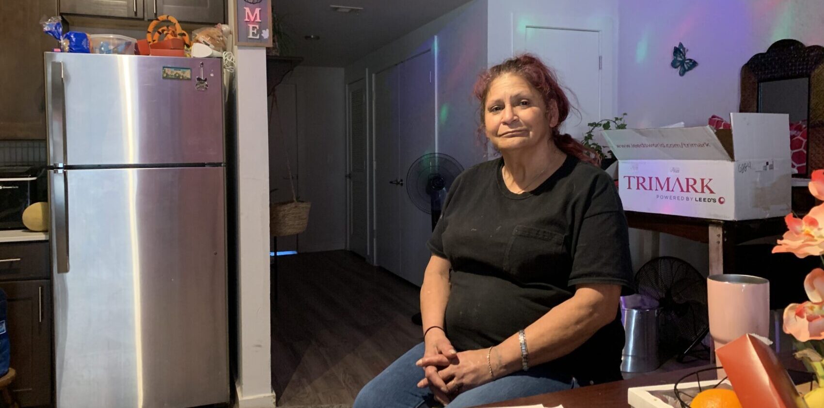 Woman sitting in kitchen beside stainless refrigerator