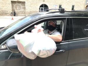 Masked person handing large bag through car window