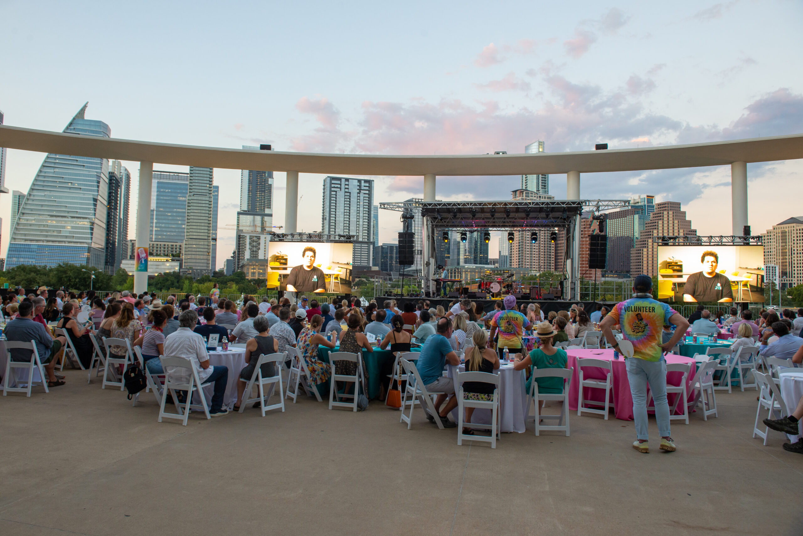 Outdoor concert with seated crowd and skyline