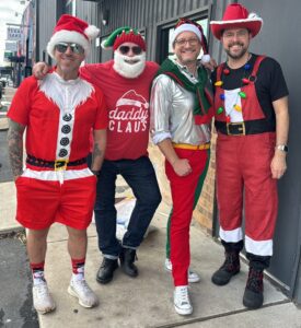 Four men wearing festive Santa and elf costumes