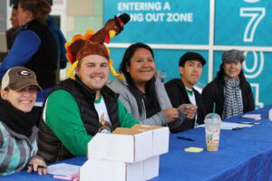 Smiling volunteers at registration table, turkey hat.