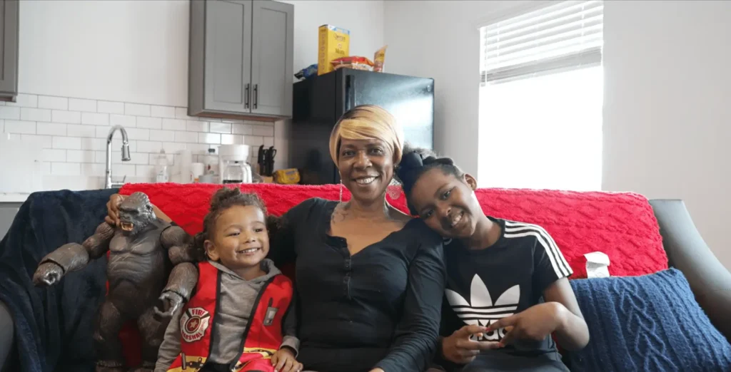 Three smiling people on couch with stuffed gorilla